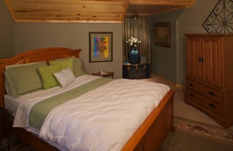 The image showcases a cozy bedroom in one of our log homes, complete with a comfortable bed and rustic wooden dresser.