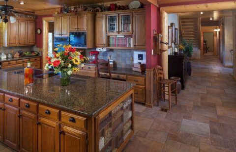 The photo shows a rustic kitchen in one of our log homes, featuring well-crafted wooden cabinets and sleek granite countertops.