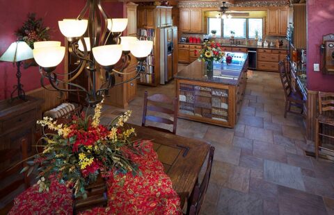 The image showcases a cozy, rustic-style kitchen in one of our log homes, complete with a wooden dining table and chairs under an elegant chandelier.