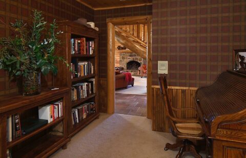 The image showcases a beautifully designed interior of our log home, featuring a hearty wooden bookcase and an elegant piano contributing to the rustic yet sophisticated ambiance.