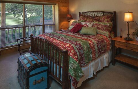 The image displays a cozy bed adorned with a vibrant, multicolored comforter, indicative of the warm and inviting atmosphere in our log homes.