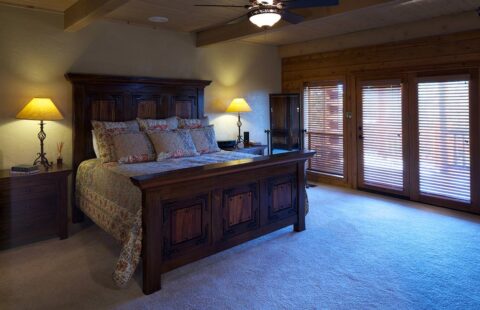 The image captures a cozy bedroom in one of our log homes featuring a comfortable bed and a charming wooden bedside table.