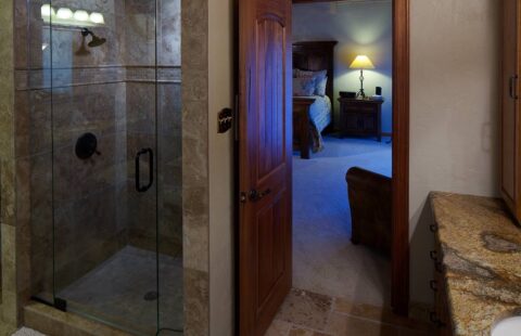 The image depicts a beautifully crafted bathroom in one of our log homes, showcasing a glass shower stall and elegant granite counter tops.
