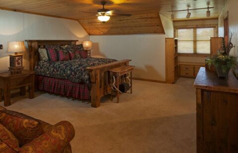 The image displays a cozy bedroom in one of our log homes, featuring a comfortable bed and a rustic wooden dresser.
