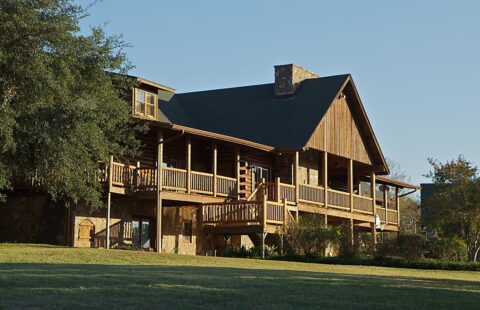 Our company produces beautifully crafted log homes, like the large house set amid a lush, grassy field in this image.