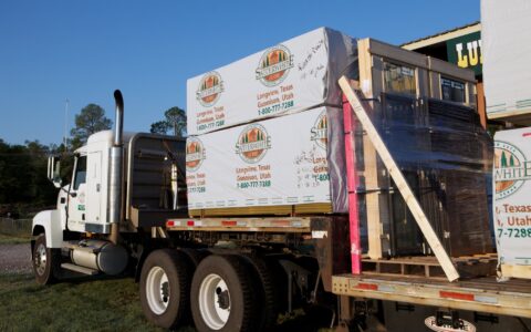 The image displays a white truck loaded with boxes, ready for delivering building materials for our log homes.